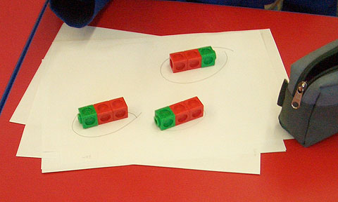 Three trains of coloured cubes, each train with two red cubes and one green, aligned with the green cube to the left in two trains and to the right in one train.